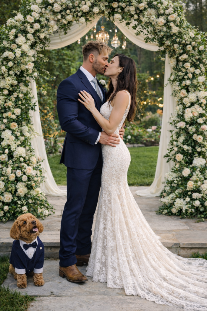 David Brackett and Juliette Fechter dream wedding standing in front of floral altar with their goldendoodle in matching tuxedo. 